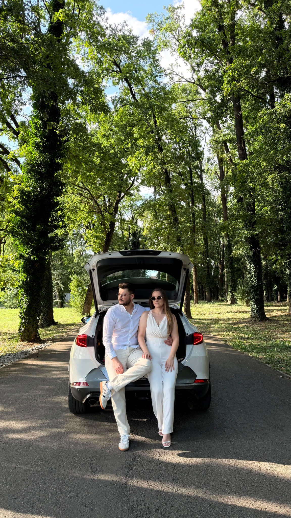 Paula și Denis stând pe portbagajul mașinii într-o alee cu copaci